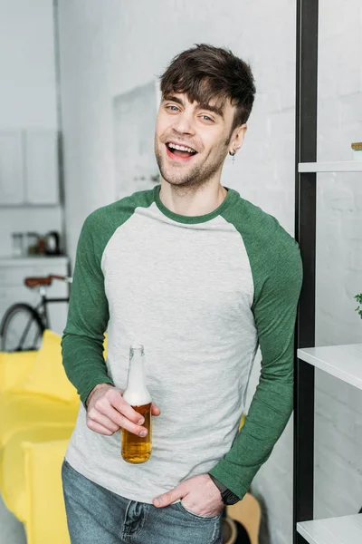 Uśmiechający Się Przystojny Mężczyzna Gospodarstwa Butelka Piwa Stojąc Przez Regały — Zdjęcie stockowe
