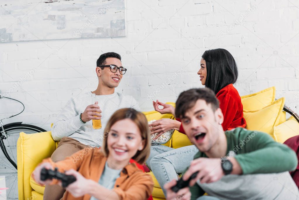 happy multicultural friends having fun at home party, playing video game and enjoying drinks and snacks 