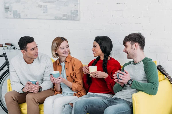 Multicultural Friends Talking Drinking Coffee While Sitting Yellow Sofa Living — Stock Photo, Image