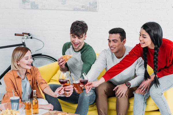 multicultural friends eating pizza and enjoying drinks at home party