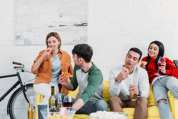 happy multicultural friends eating pizza and enjoying drinks at home party