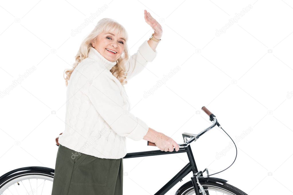 cheerful senior woman waving hand near bicycle isolated on white