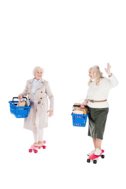 happy senior woman riding penny board and waving hand to friend holding shopping basket idolated on white clipart