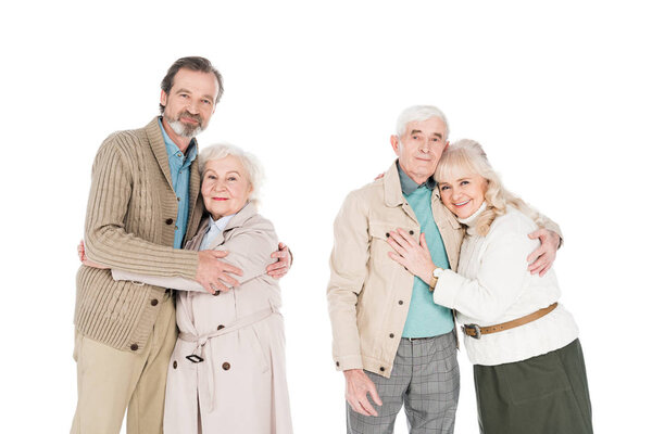 cheerful retired couples hugging and smiling isolated on white