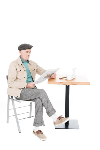 retired man reading newspaper while sitting on chair with crossed legs isolated on white