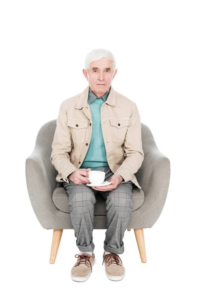 retired man sitting in armchair with cup of tea isolated on white