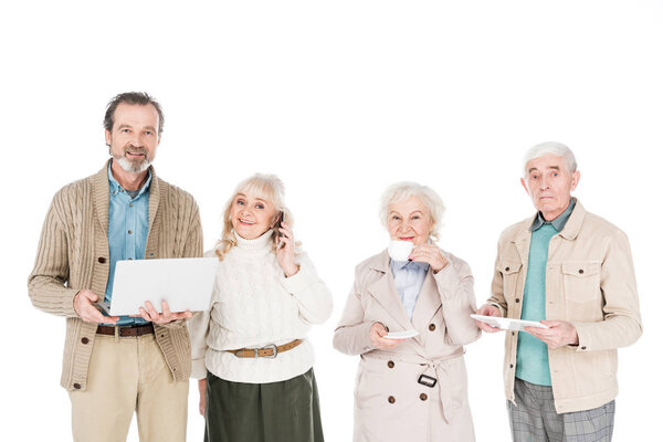 senior people standing with gadgets near woman drinking tea from cup isolated on white