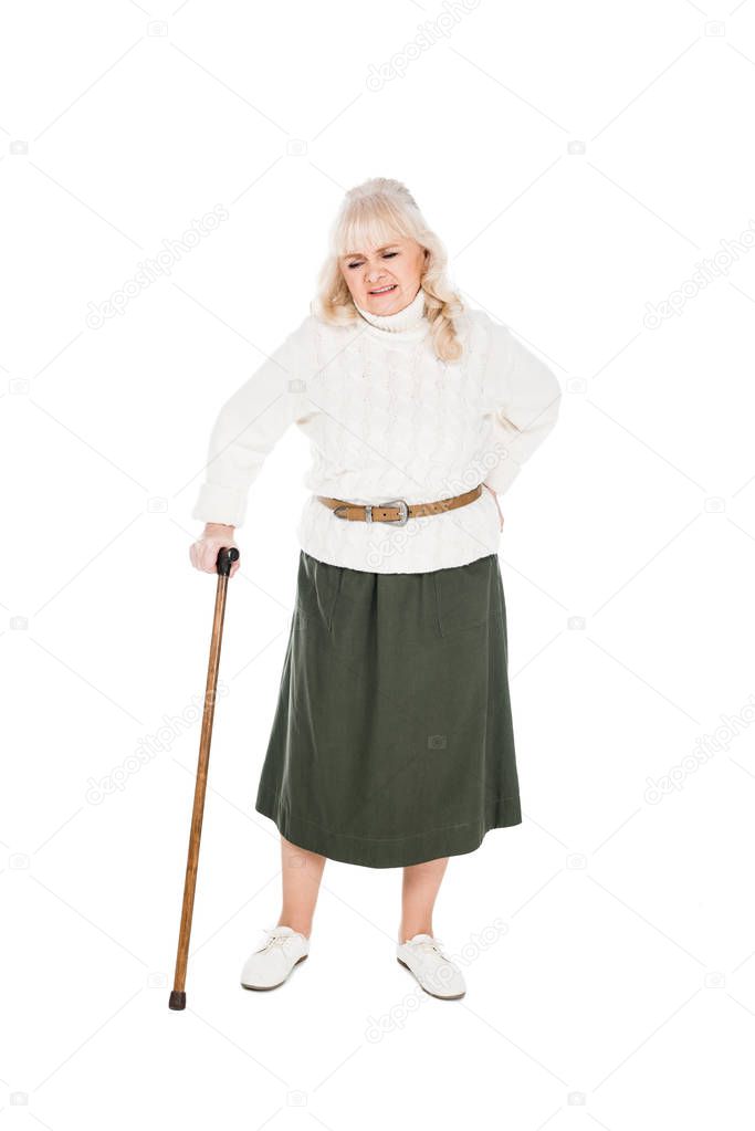 senior woman holding back while having arthritis pain and standing with walking cane isolated on white