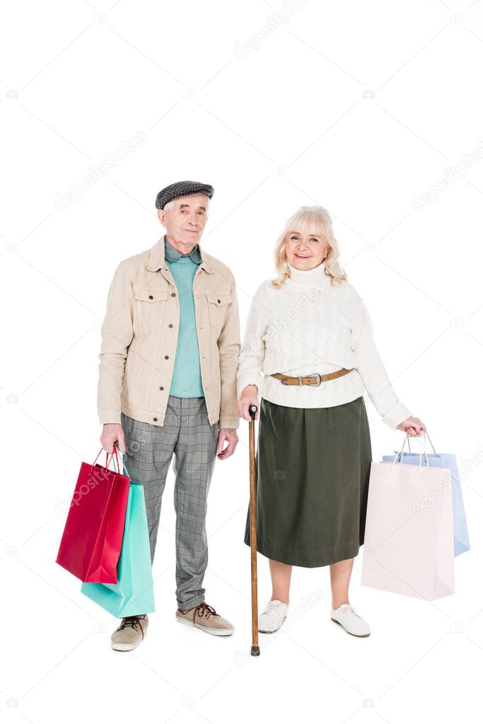 cheerful retired couple standing with shopping bags isolated on white