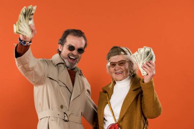 Doları banknot tutarak ve izole üzerinde turuncu gülümseyen mutlu emekli çift
