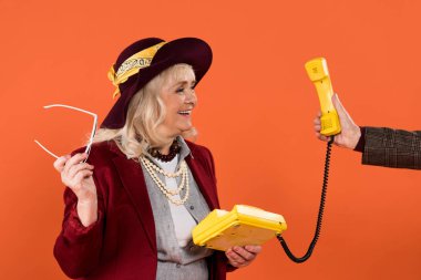 emekli adam retro telefon üzerinde turuncu izole kadın kıdemli neşeli yakınındaki elinde tutarak kırpılmış görünümünü 
