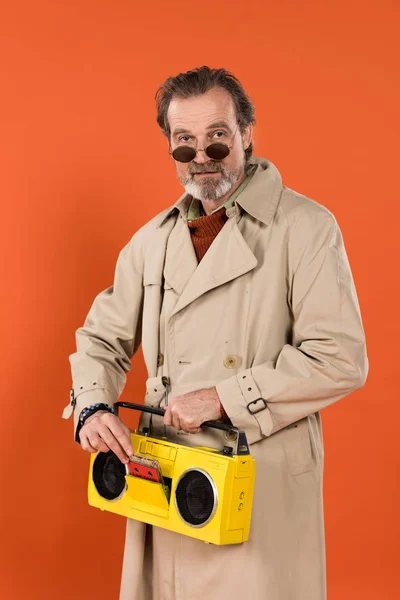 オレンジに分離された手で黄色のラジカセを保持してスタイリッシュな引退した男 — ストック写真