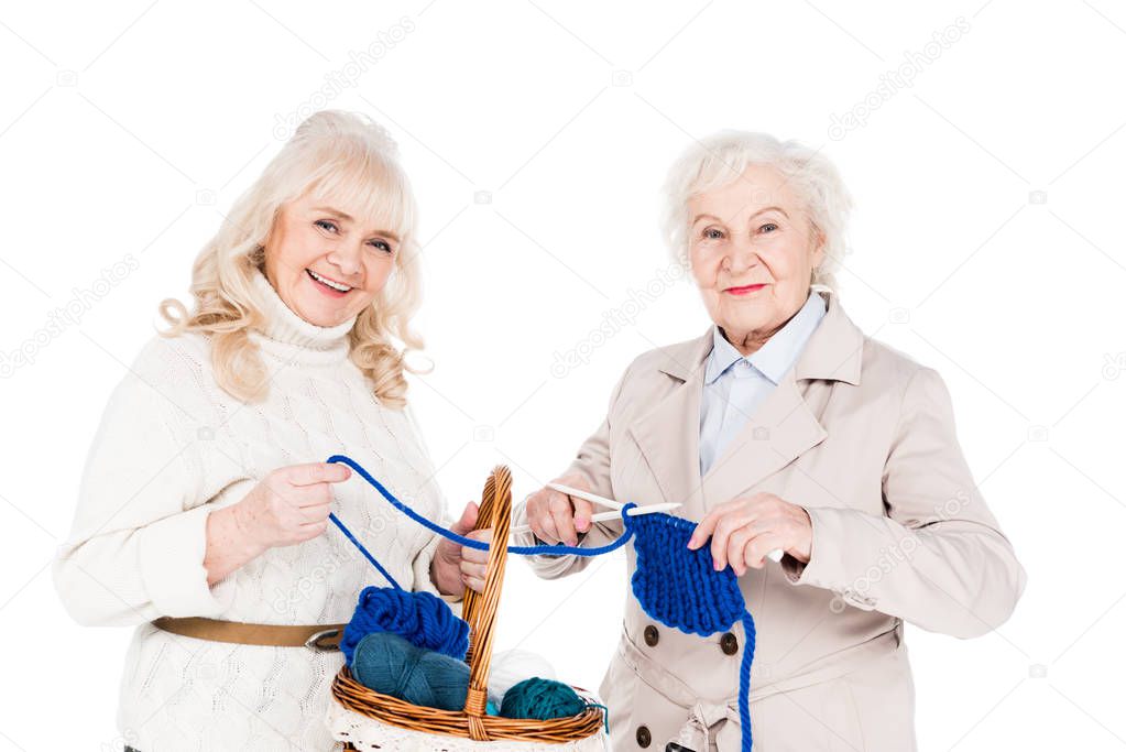 happy retired woman knitting near friend holding basket isolated on white