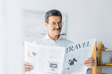 cheerful senior man reading travel newspaper at home clipart