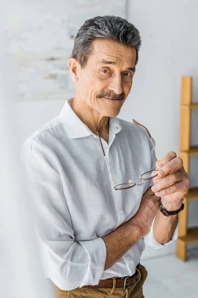 Homem Sênior Feliz Segurando Óculos Sorrindo Casa — Fotografia de Stock