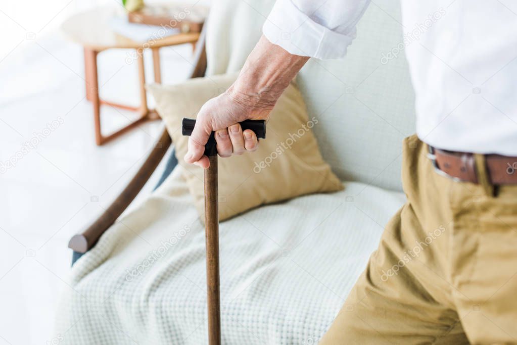 cropped view of senior man holding walking cane near sofa