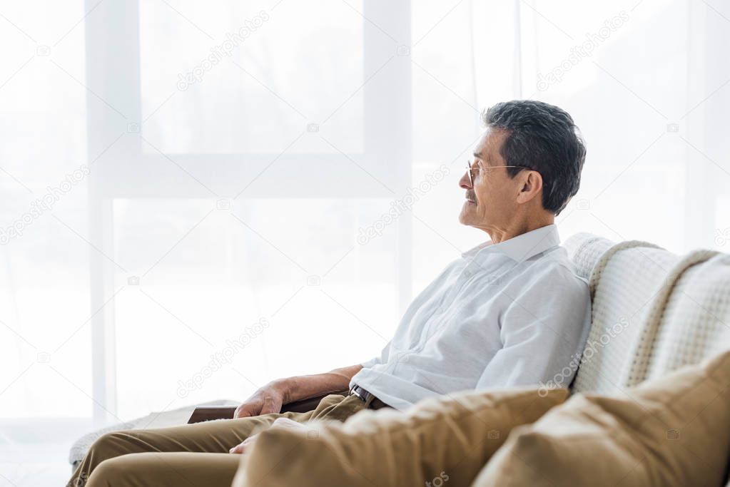 thoughtful senior man sitting on sofa at home