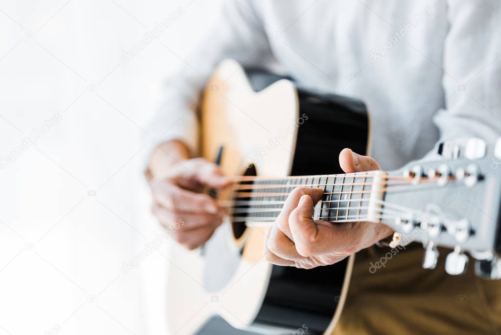 cropped view of senior man playing acoustic guitar at home