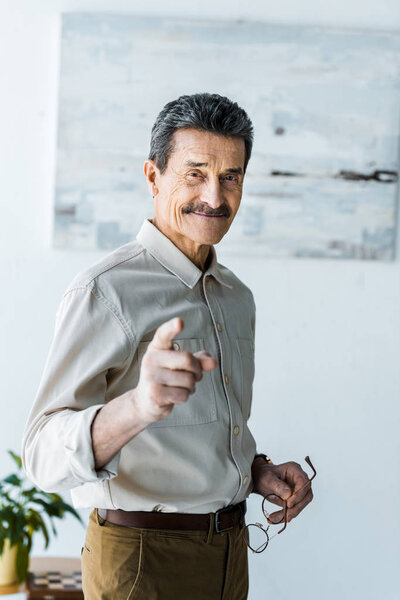 cheerful senior man pointing with finger and holding glasses