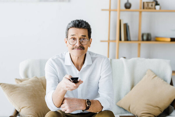 cheerful senior man sitting on sofa and holding remote control in hand