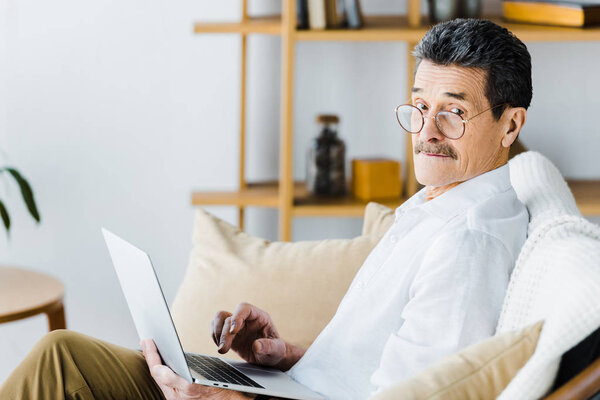 surprised senior man using laptop while sitting on sofa