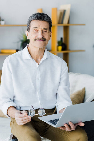 cheerful pensioner with mustache using laptop at home