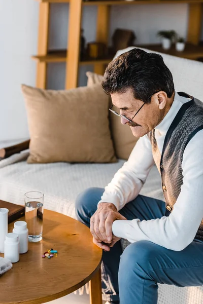 Uomo Anziano Guardando Pillole Bicchiere Acqua Sul Tavolino — Foto Stock