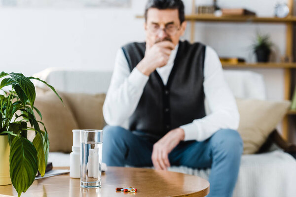selective focus of pills near glass of water with senior man on background