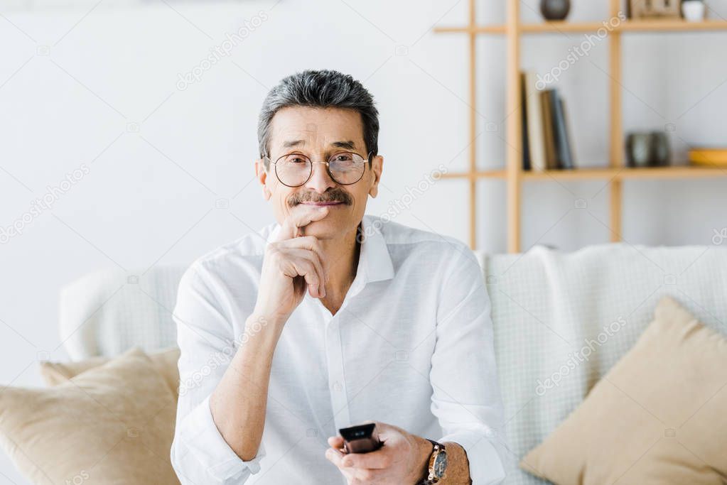 cheerful senior man with mustache sitting on sofa and holding remote control