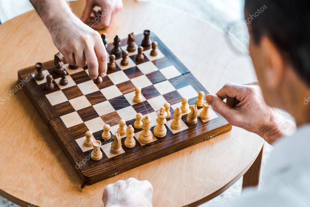 selective focus of wooden chess board with retired men playing chess at home