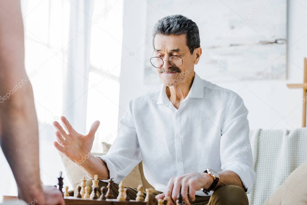selective focus of senior man with mustache playing chess with friend at home