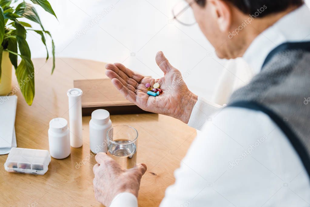 selective focus of senior man looking at pills while holding glass of water