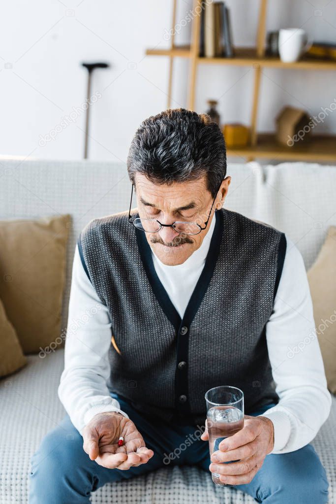 retired man looking at pills while holding glass of water at home