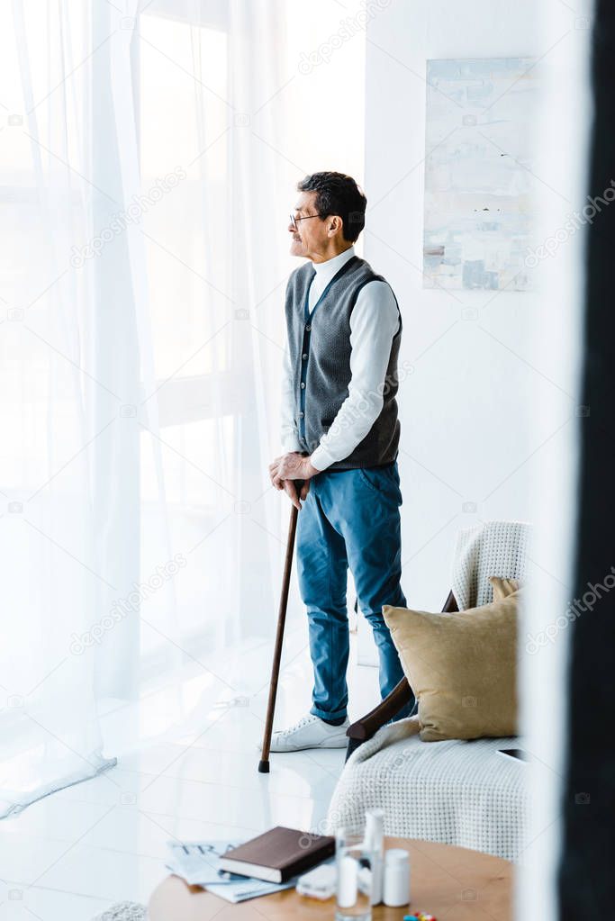 retired man standing with walking stick at home