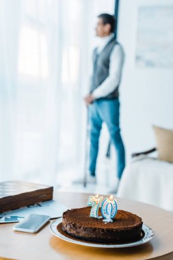 selective focus of birthday cake with burning candles with lonely senior man standing with  walking cane on background clipart