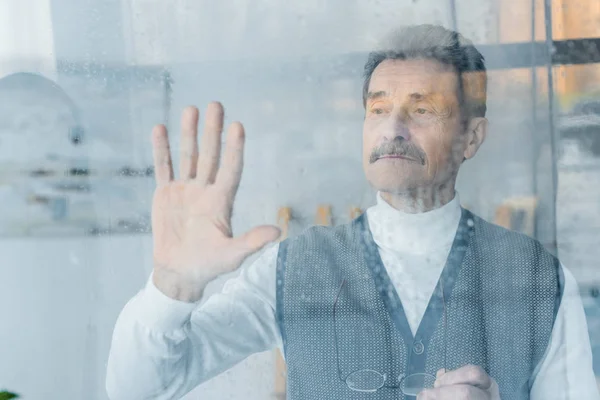 Sad Senior Man Waving Hand While Standing Window — Stock Photo, Image