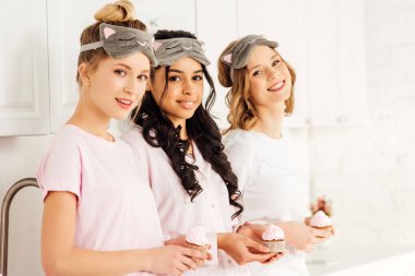 güzel pijama partisi sırasında cupcakes tutarak maskeler uyku çok ırklı kızlar gülümseyen