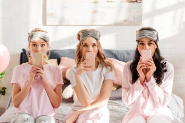 pijama partisi sırasında yatak ve akıllı telefonlar ile kaplama ağız oturan maskeleri uyku çok kültürlü güzel kızlar