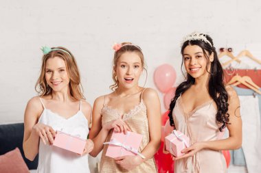güzel pembe hediye kutuları tutarak ve pijama partisi sırasında kameraya bakarak kıyafeti çok kültürlü kızlarda gülümseyen