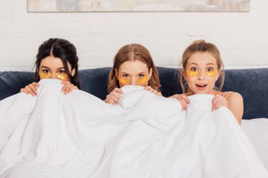 çok kültürlü kızlarla güzel pijama partisi sırasında kamera yatakta bakarak altın göz yamalar