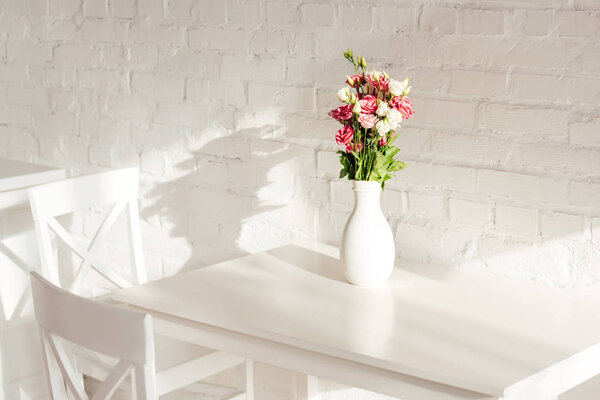 flower bouquet in vase on white table with chairs and brick wall in kitchen
