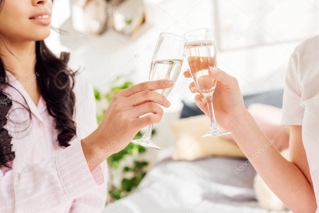 cropped view of multicultural girls clinking champagne glasses at home