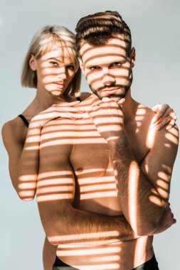 young woman hugging confident shirtless man isolated on grey with shadows clipart