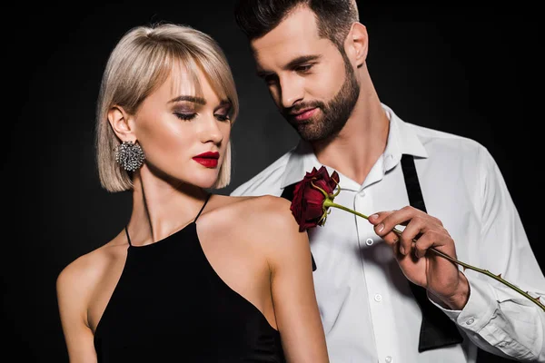 充满激情的男人触摸优雅的女人与红玫瑰的肩膀 孤立的黑色 — 图库照片