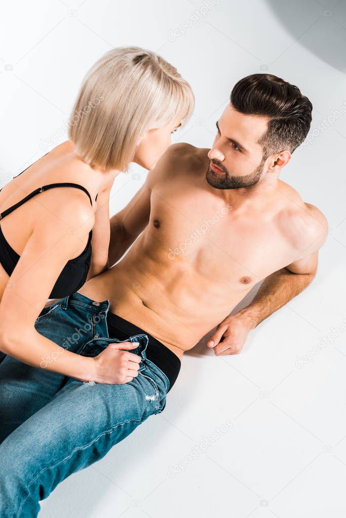 seductive young couple in underwear and jeans lying on grey