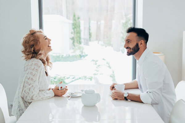Blissful couple laughing while drinking coffee together