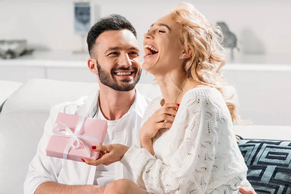 Happy Laughing Girl Sitting Sofa Boyfriend Holding Present — Stock Photo, Image