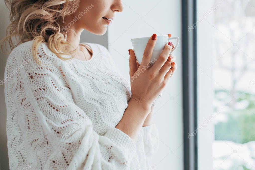 Cropped view of woman in knitted sweater drinking coffee