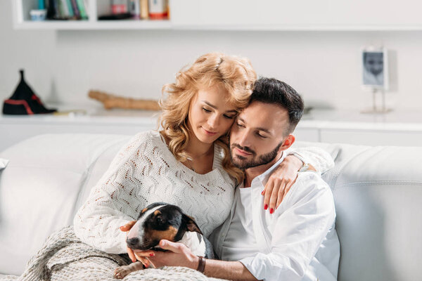 Blissful couple embracing while sitting on sofa with dog