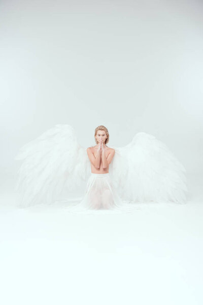 Beautiful woman with angel wings doing praying gesture and looking at camera isolated on white